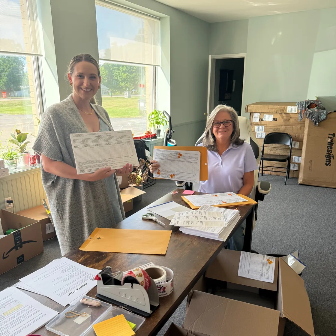 Two members of a VFO team reviewing and packaging completed petition sheets at a work table.